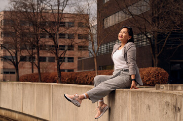 Young woman sitting on concrete ledge enjoying sunshine in urban park setting.