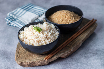 raw and cooked brown rice with a rock block background. 