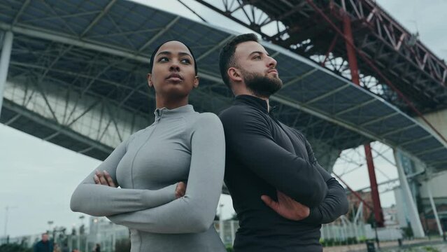 A diverse fitness duo exudes confidence while posing outdoors under a large bridge, representing teamwork and determination.