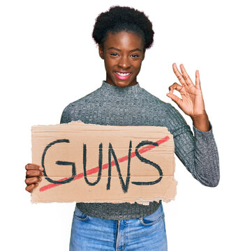 Young african american girl holding no guns warning banner doing ok sign with fingers, smiling friendly gesturing excellent symbol