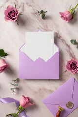 Violet paper envelope with blank paper card inside, roses flowers on marble background. Wedding stationery set top view.