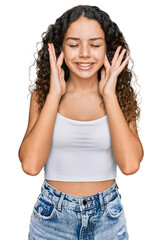 Teenager hispanic girl wearing casual clothes covering ears with fingers with annoyed expression for the noise of loud music. deaf concept.