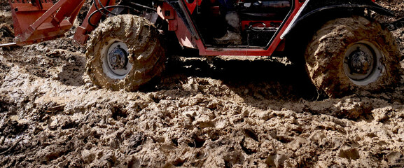 A work tractor with wheels and tires full of mud on a country road - 768038337