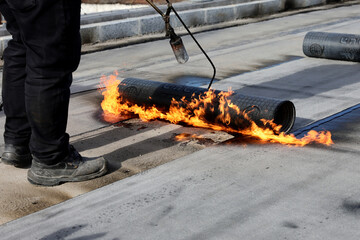 Professional construction workers using a blowtorch to glue modified bitumen roll sheet over a concrete road.