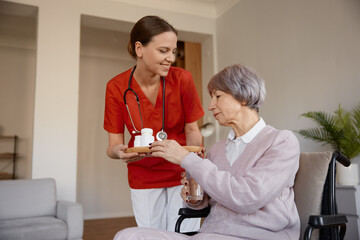 Senior lady receiving pills from woman healthcare worker at nursing home - obrazy, fototapety, plakaty