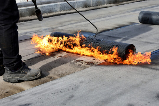 Professional construction workers using a blowtorch to glue modified bitumen roll sheet over a concrete road.
