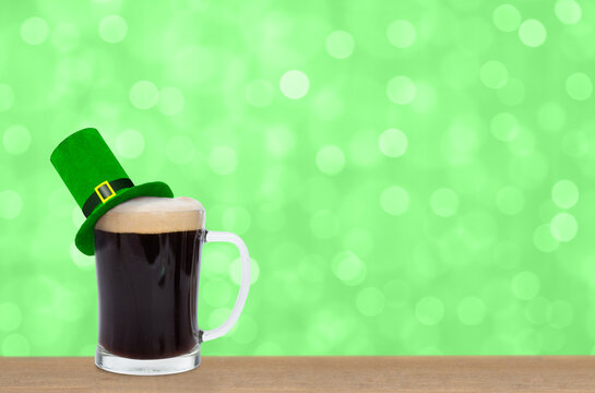 Glass of black beer with green top hat on green blurred background. Saint Patrick's Day Concept. Empty space for text