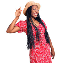 Young african american woman wearing summer hat waiving saying hello happy and smiling, friendly welcome gesture