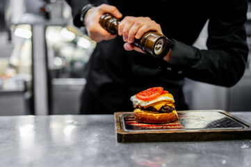 A chef adds pepper to a gourmet burger, the final touch in its preparation process, making it...