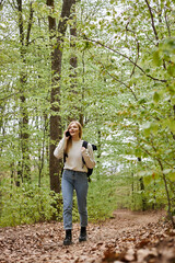 Pretty blonde woman traveler with backpack talking by phone walking in forest scenery - obrazy, fototapety, plakaty