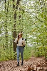 Zelfklevend Fotobehang Pretty blonde woman traveler with backpack talking by phone walking in forest scenery © LIGHTFIELD STUDIOS