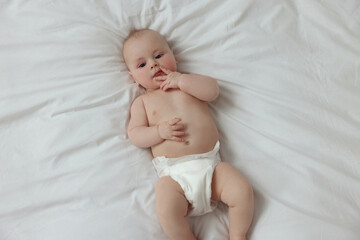 Cute little baby in diaper lying on white bed, top view