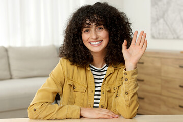 Happy woman waving hello at wooden table in room © New Africa
