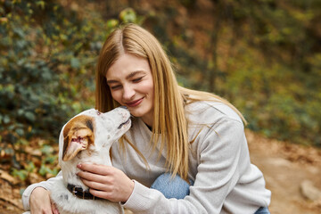 Emotional woman kissing and hugging her cute white dog and making funny face in forest