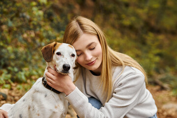 Smiling woman hugging gently her dog companion with eyes closed at forest backpacking trip