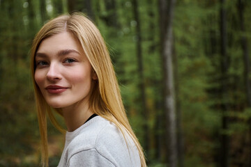Smiling cheerful beautiful blonde woman looking at the camera while walking in forest