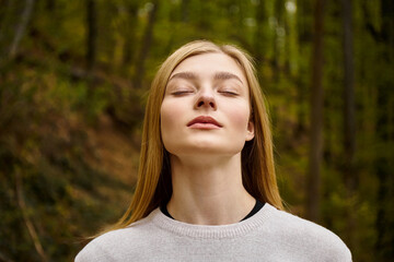 Relaxed blonde woman breathing fresh air in forest on solo hiking trip, closed eyes portrait