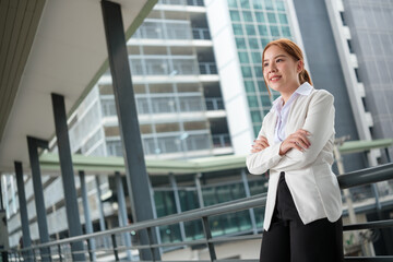 Portrait of a happy Asian Businesswoman with arms crossed and looking at the left standing near her office, with a big building background.