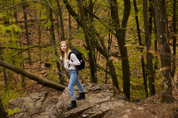 Blond calm pretty woman hiker with backpack walking through a forest looking at camera