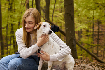 Gentle forest scene with a blonde woman explorer hugging her dog, caring for her pet's comfort