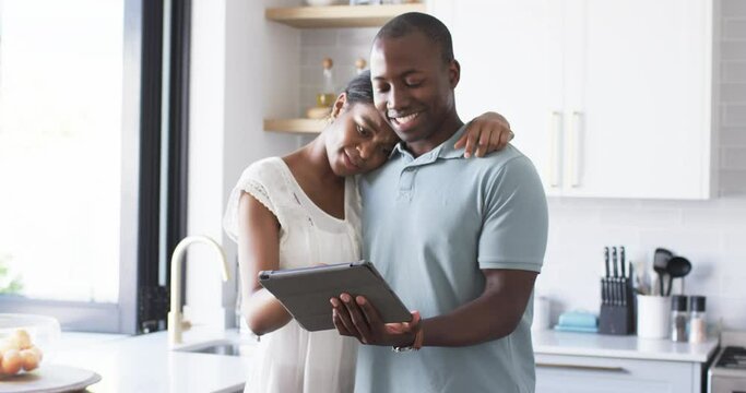 A diverse couple is using a tablet in the kitchen at home