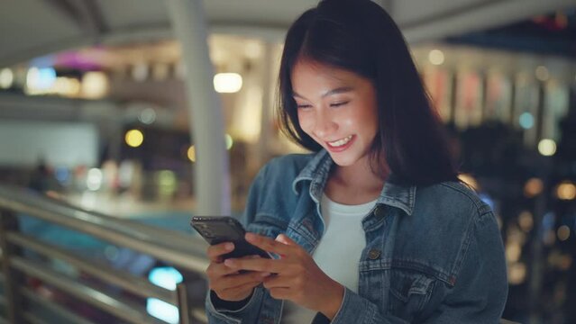 Happy young asian woman chatting on mobile phone while standing in city at night, Female using smartphone enjoy spend time on after worked
