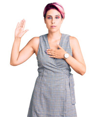 Young beautiful woman with pink hair wearing casual clothes swearing with hand on chest and open...