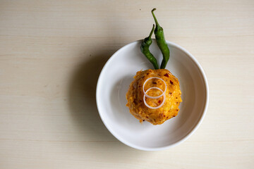 Traditional Bengali food Aloo Bharta on a white bowl with green chilli peppers and onion rings on wooden background. Top view