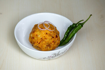 Delicious Aloo Bharta on a white bowl with green chilli peppers and onion rings on wooden background. It is traditional Bengali (Bangladeshi) food. 