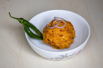 Tasty Aloo Bharta on a white bowl with green chilli peppers and onion rings on wooden background. It is traditional Bengali (Bangladeshi) food. 