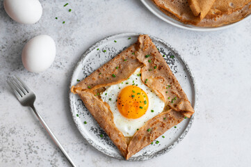 Homemade buckwheat crepes. Galettes Bretonnes with cheese and fried egg on a grey background. Traditional French cuisine.