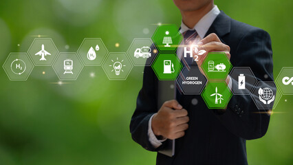 A businessman uses a virtual screen to illustrate green hydrogen production and usage, with icons...