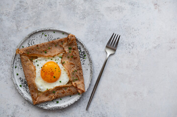 Homemade buckwheat crepes. Galettes Bretonnes with cheese and fried egg on a grey background. Traditional French cuisine.