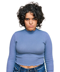 Young hispanic woman with curly hair wearing casual clothes skeptic and nervous, frowning upset...