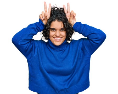 Young hispanic woman with curly hair wearing turtleneck sweater posing funny and crazy with fingers on head as bunny ears, smiling cheerful