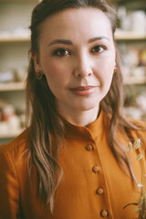 Close-up portrait of an elegant woman against the background of shelves with ceramic dishes. Elegant woman ceramic artist in a cozy studio Head shot, atmospheric portrait