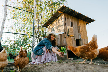 Smiling woman enjoying farm life while feeding her chickens. Happy red-haired woman enjoying feeding chickens in the garden of a rural estate