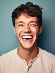 A young man laughing heartily against a blue background