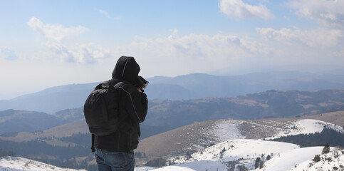 hiker with backpack and jacket looks at the view from the summit of the snow-capped mountain in the...