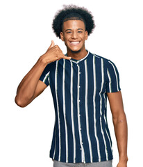 Fototapeta na wymiar African american man with afro hair wearing casual clothes smiling doing phone gesture with hand and fingers like talking on the telephone. communicating concepts.