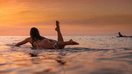 Candid view of a woman surfer heading out to catch waves at sunset - 768074333