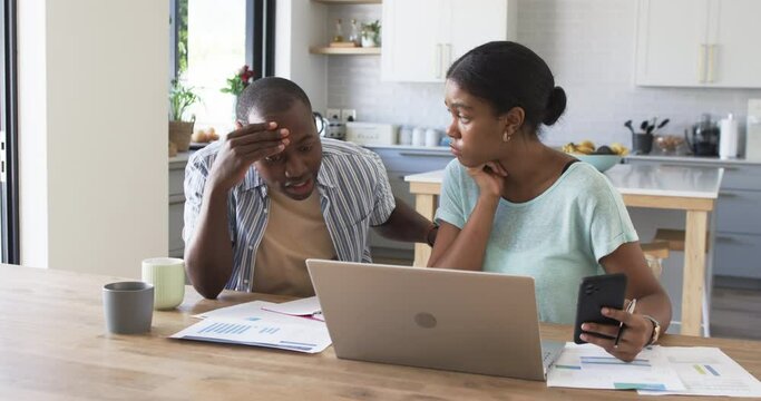 A young African American couple is managing finances at home using a laptop