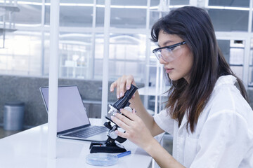 female doctor student examining and analysis virus test sample on microscope. young biotechnology specialist working in lab. medical science laboratory hospital.