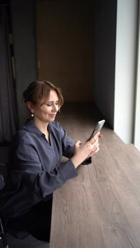 a  beautiful middle age business woman wearing gray shirt, wide leg pants abd black stilettos make video for a stories in moders workspase in tall building