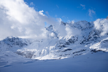Snow covered mountain top with clouds and blue sky 