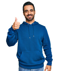 Young hispanic man wearing casual clothes smiling happy and positive, thumb up doing excellent and...