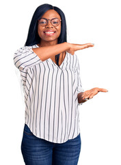 Young african american woman wearing casual clothes and glasses gesturing with hands showing big and large size sign, measure symbol. smiling looking at the camera. measuring concept.