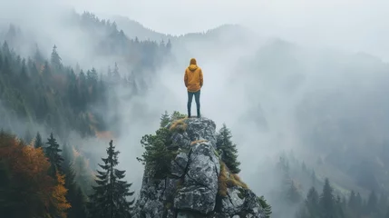 Fotobehang Solitary person standing on a rock, surrounded by a foggy mountainous landscape © Robert Kneschke