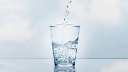 pouring drinking water in a transparent glass isolated on abstract background with glass table,...