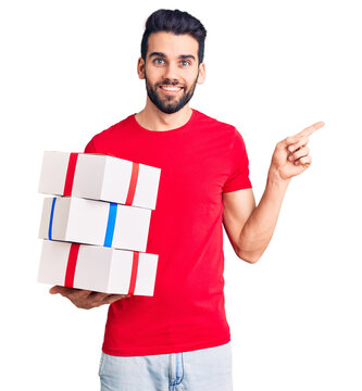 Young handsome man with beard holding gift smiling happy pointing with hand and finger to the side